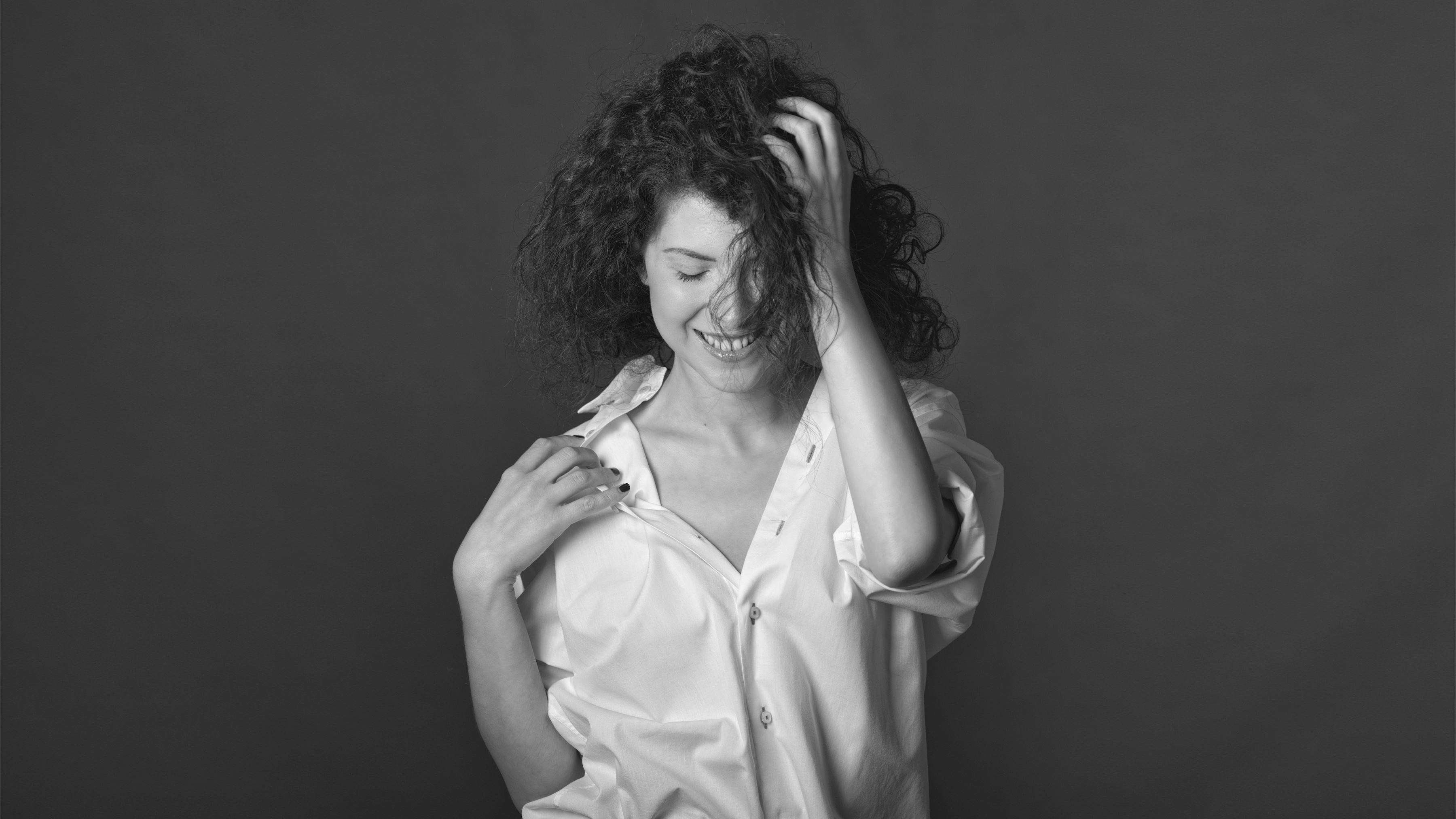 Black and white portrait of a smiling model on a dark grey background wearing a white shirt