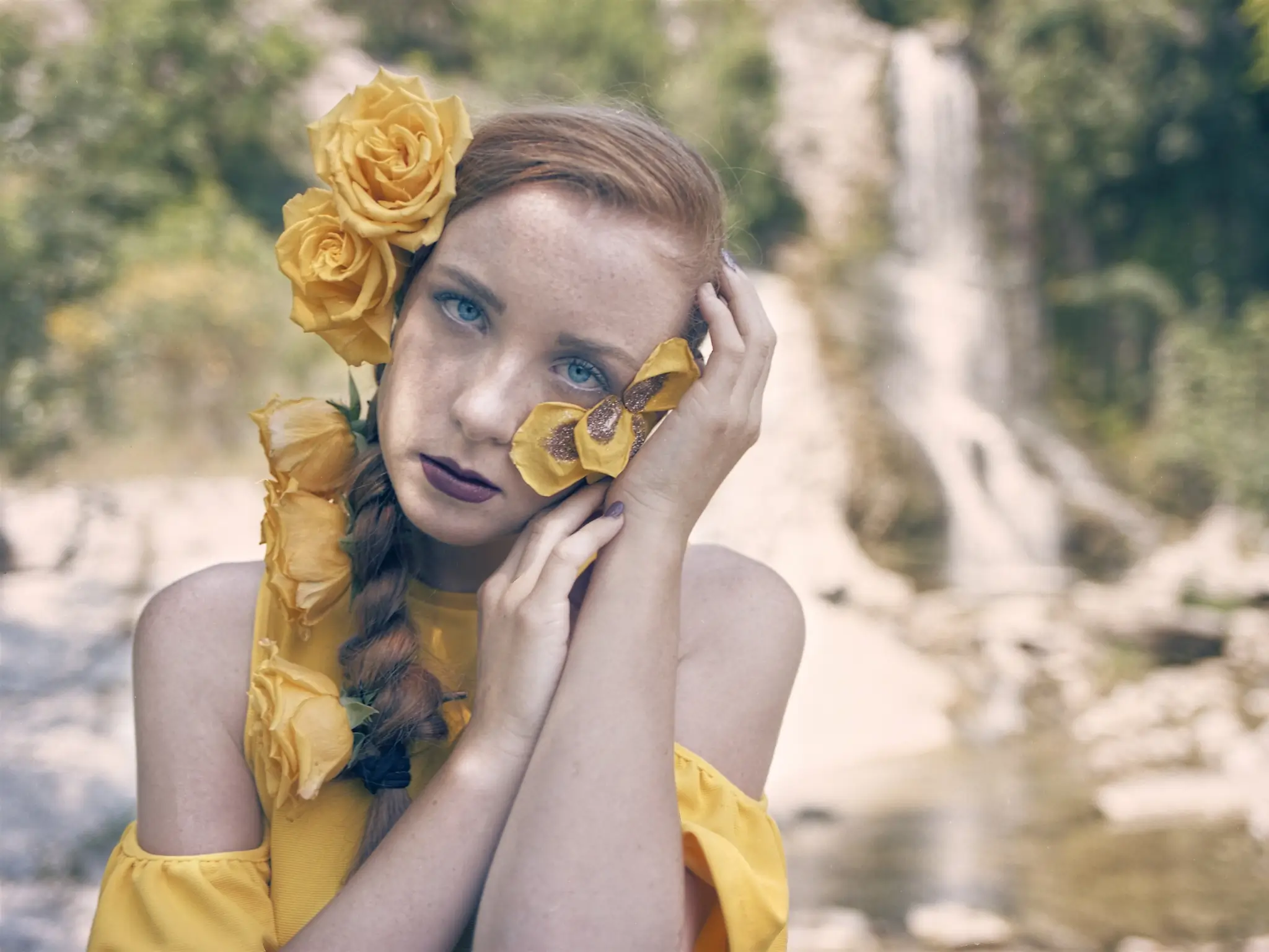 Oudoors portrait of a model with yellow roses in the hair and a waterfall on the background